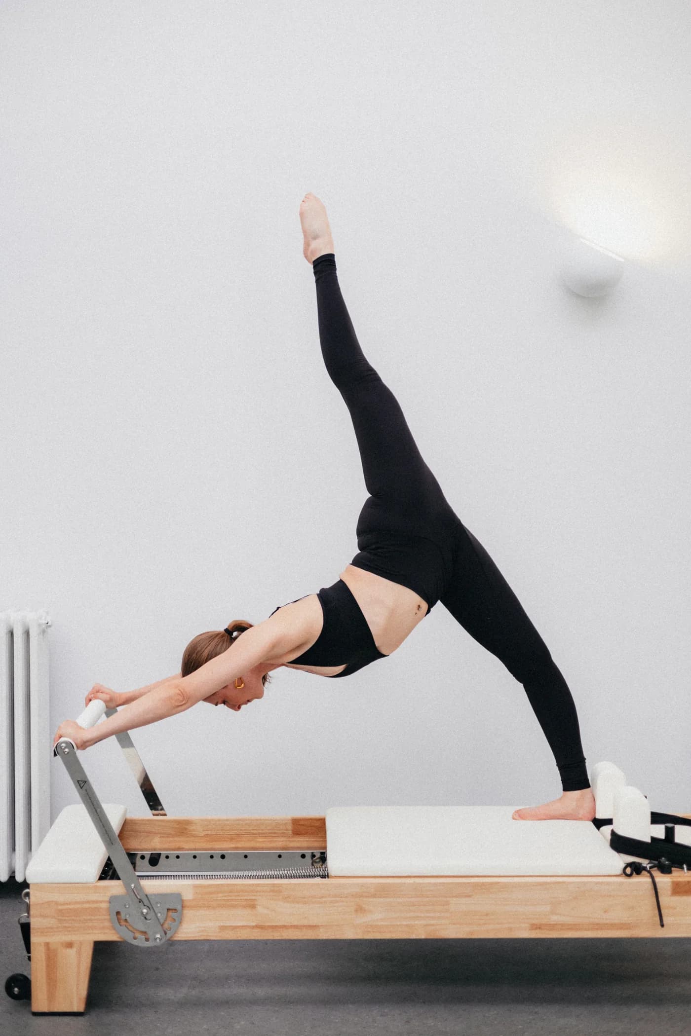 Pauline en équilibre sur le Reformer, une jambe tendue vers le plafond